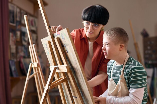 Foto un niño sonriente con síndrome de down sentado junto a un caballete en la clase de arte