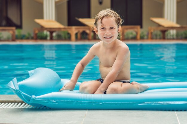 Niño sonriente sobre un colchón inflable azul en la piscina