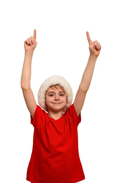 Niño sonriente con sombrero de Santa señala con los dedos hacia arriba. Aislar