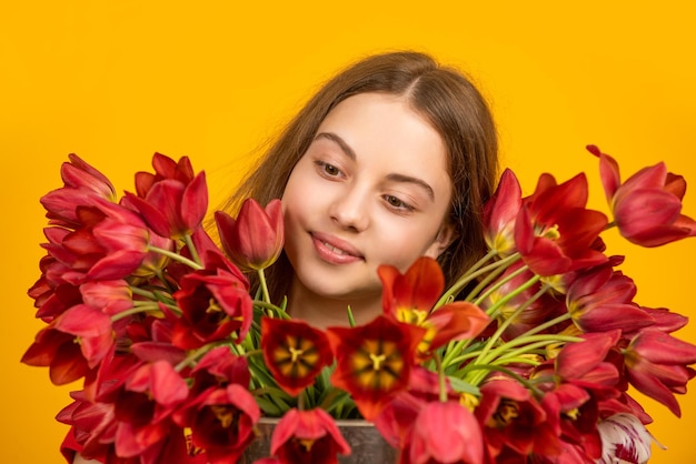 Niño sonriente sostiene flores de tulipán de primavera sobre fondo amarillo