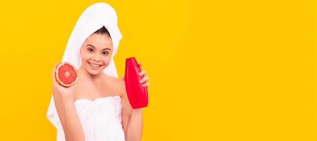 Niño sonriente en toalla con botella de champú de pomelo sobre fondo amarillo Cosméticos y cuidado de la piel para diseño de póster de niño adolescente Banner de niña de belleza con espacio de copia