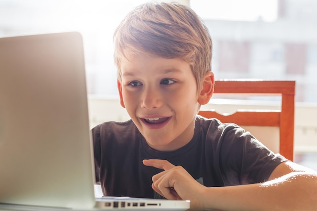 Un niño sonriente usando una computadora portátil en la mesa de casa