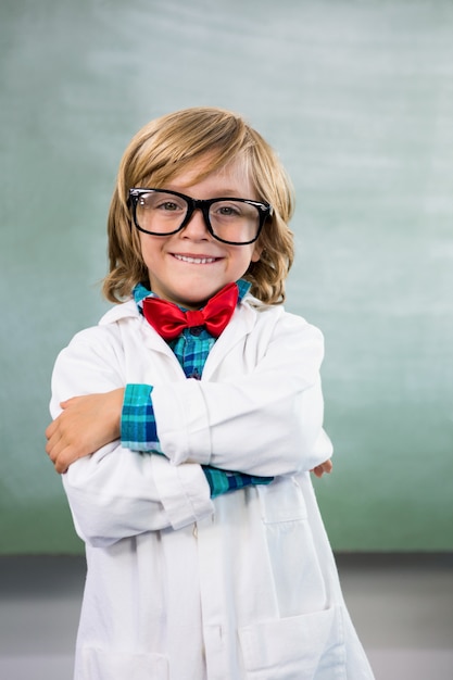 Niño sonriente vestido como científico de pie en el aula