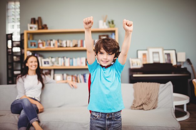 Niño sonriente vistiendo traje de superhéroe con madre sentada en el sofá