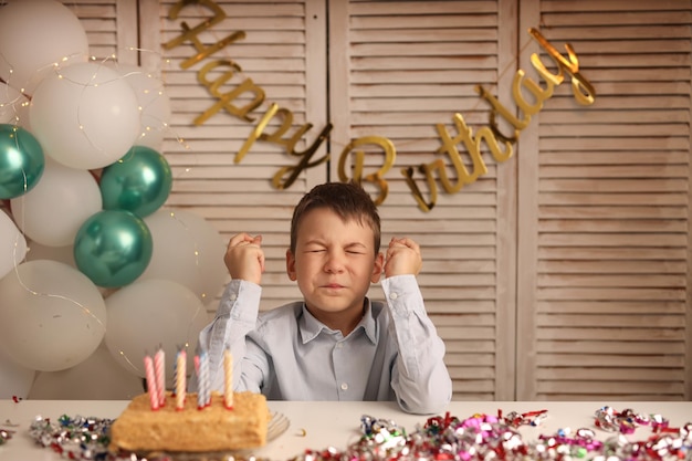 El niño sopla las velas de la tarta de cumpleaños y pide un deseo bolas con una guirnalda en el