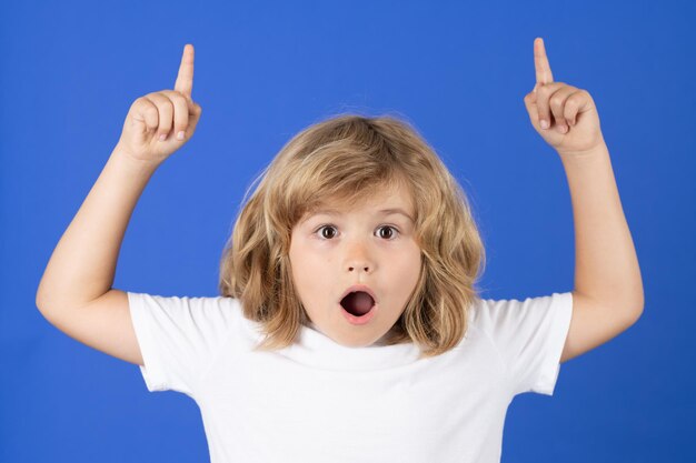 Niño sorprendido apuntando con el dedo sobre el fondo azul del estudio