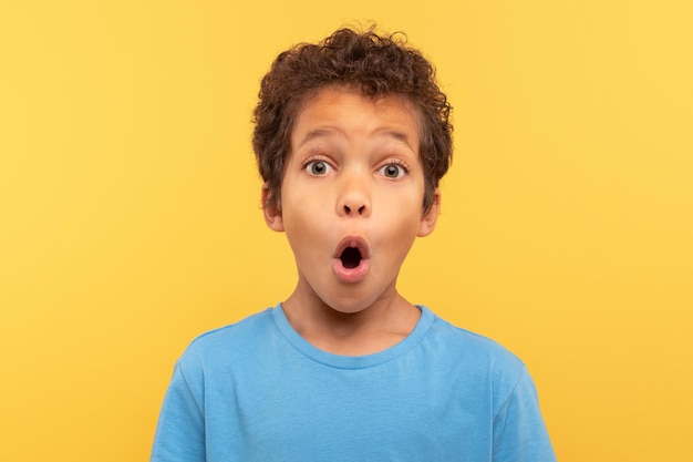Niño sorprendido con la boca abierta mirando el fondo amarillo de la cámara