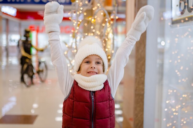 Niño sorprendido con gorro y bufanda blancos en el centro comercial cerca de la vitrina