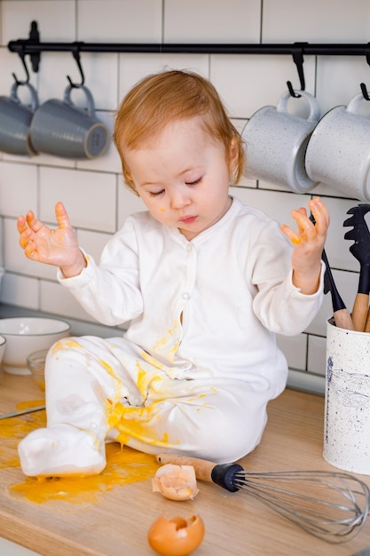 Un niño sorprendido haciendo lío en la cocina rompiendo huevos jugando con ingredientes alimentarios