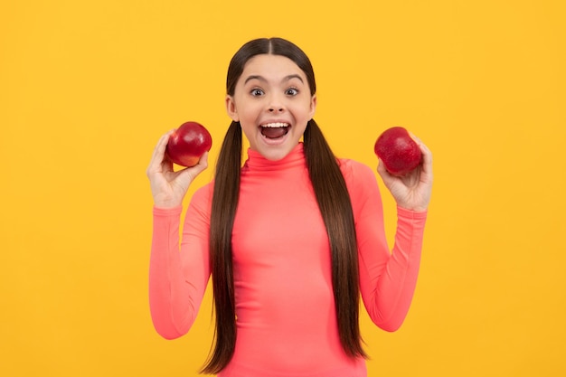 Niño sorprendido con manzana roja sobre fondo amarillo haciendo dieta