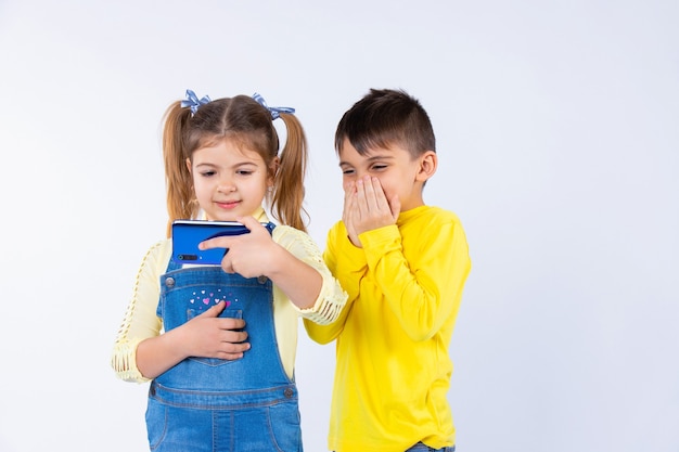 Niño sorprendido sobre un fondo blanco sentado junto a una niña con un teléfono inteligente.