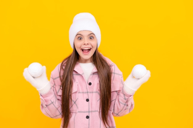 Niño sorprendido con sombrero y mitones jugando bolas de nieve en la infancia de fondo amarillo