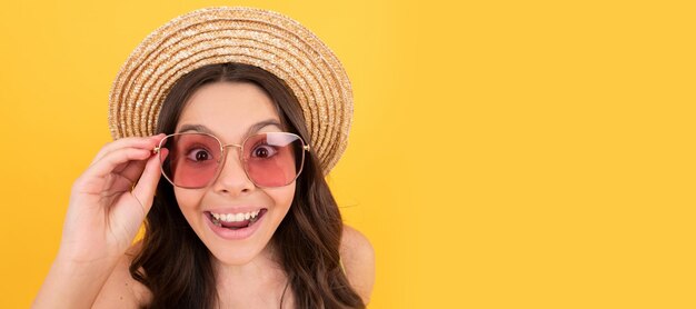 Niño sorprendido en sombrero de paja de verano y gafas tiene cabello rizado sobre fondo amarillo ventas de verano Cara de niño cartel horizontal adolescente niña aislado retrato banner con espacio de copia