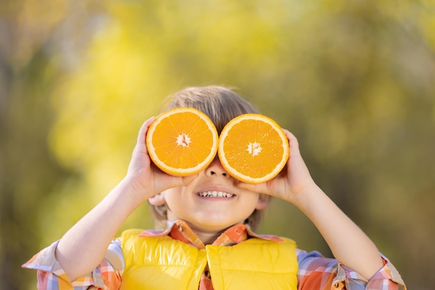 Niño sorprendido sosteniendo rodajas de naranja en el parque de otoño