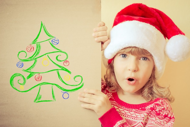 Niño sorprendido con tarjeta de Navidad con árbol de Navidad dibujado. Concepto de vacaciones de invierno