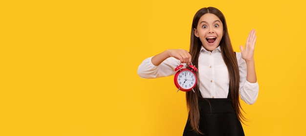 Niño sorprendido en uniforme escolar con reloj de alarma que muestra la hora en el tiempo de fondo amarillo Niño adolescente con alarma de reloj cartel horizontal Espacio de copia de encabezado de banner