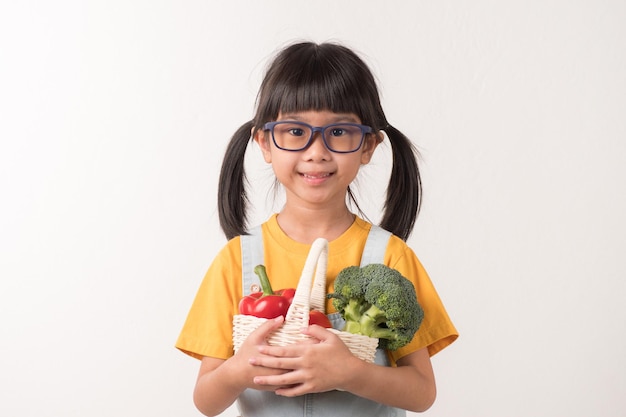 Niño sostenga la cesta de verduras. Linda chica le encanta comer vegetales.