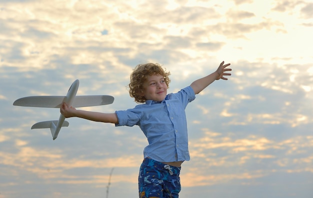Niño sosteniendo un avión de juguete contra el cielo durante la puesta de sol