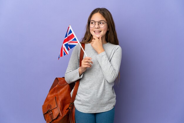 Niño sosteniendo una bandera del Reino Unido sobre antecedentes aislados mirando hacia el lado y sonriendo