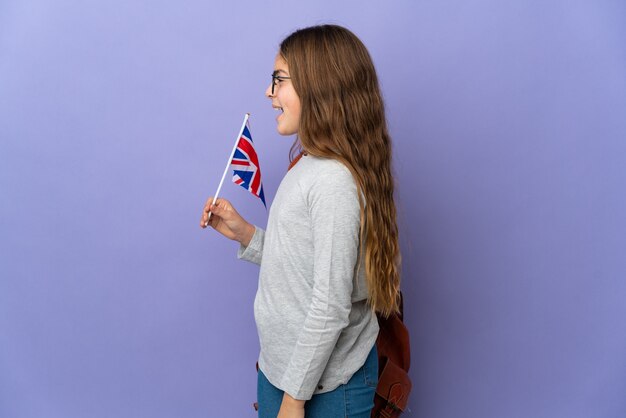 Niño sosteniendo una bandera del Reino Unido sobre una pared aislada riendo en posición lateral