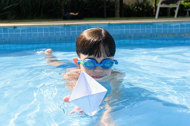 Niño sosteniendo un barco de papel en la piscina en un día de verano.