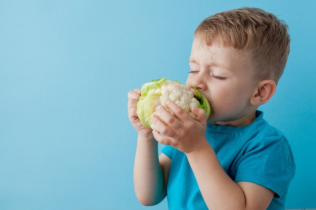 Niño sosteniendo el brócoli en sus manos sobre azul, dieta y ejercicio para una buena salud