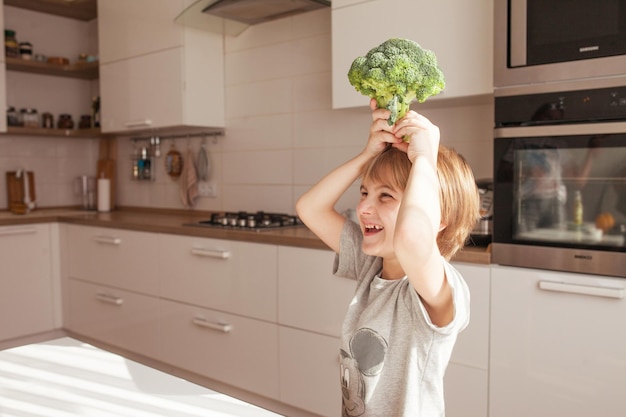 Niño sosteniendo brócoli verde Concepto de comida saludable Nutrición infantil Verduras frescas en manos de un niño alegre