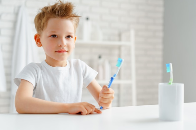 Niño sosteniendo el cepillo de dientes en la mano de pie en el baño.