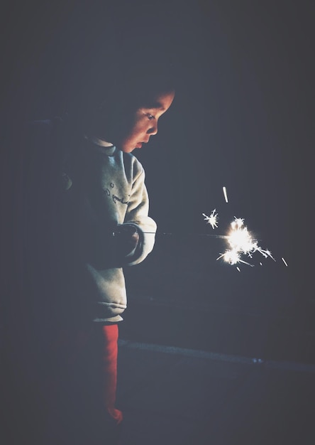 Foto niño sosteniendo una chispa ardiente durante el año nuevo chino por la noche.