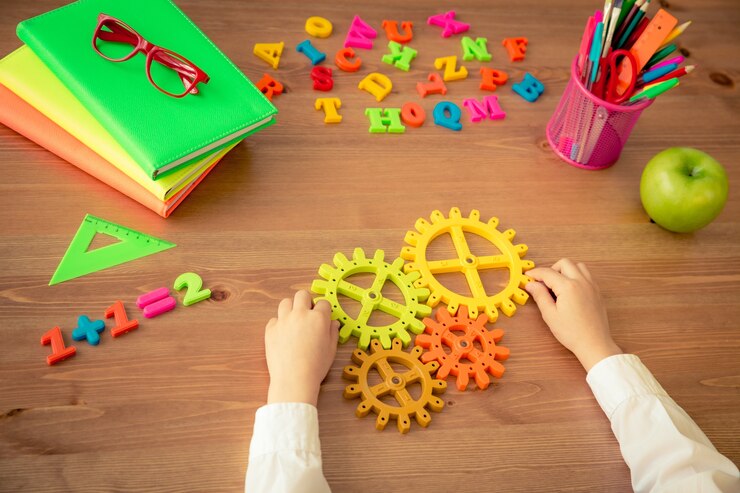 Foto niño sosteniendo el engranaje en las manos. artículos escolares en el escritorio de madera en clase. concepto de educación. vista superior