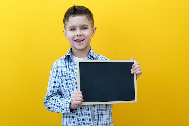 Niño sosteniendo una hoja de tablero Lindo niño pequeño con espacio de copia de fondo amarillo de pizarra