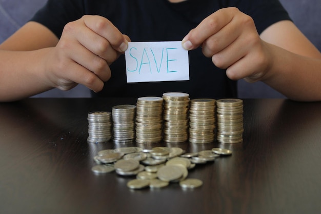 niño sosteniendo un papel con la inscripción guardar y monedas en la mesa