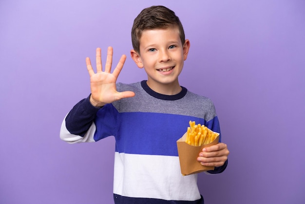 Niño sosteniendo patatas fritas aisladas en un fondo morado contando cinco con los dedos