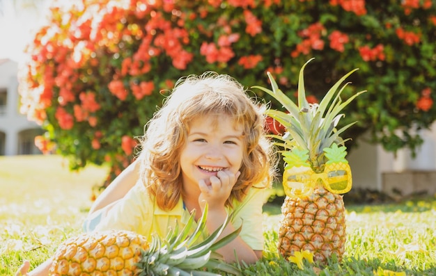 Niño sosteniendo una piña posando fondo de naturaleza de verano con espacio de copia Concepto de frutas saludables para niños