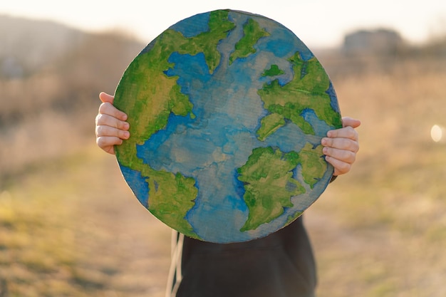 Niño sosteniendo el planeta en las manos contra el fondo verde de la primavera día de la tierra