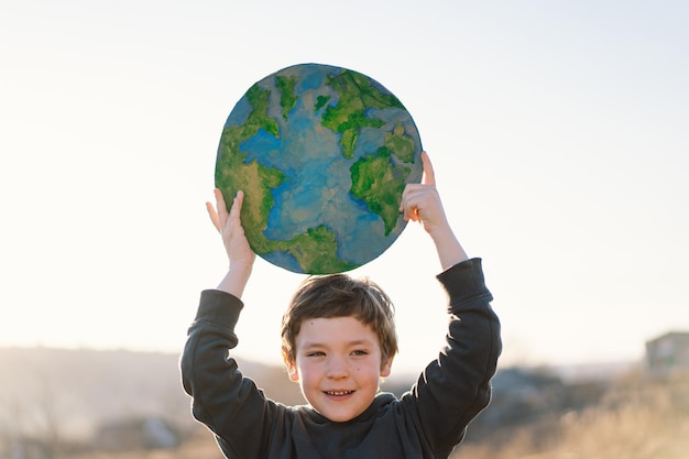 Niño sosteniendo el planeta en las manos contra el fondo verde de la primavera día de la tierra