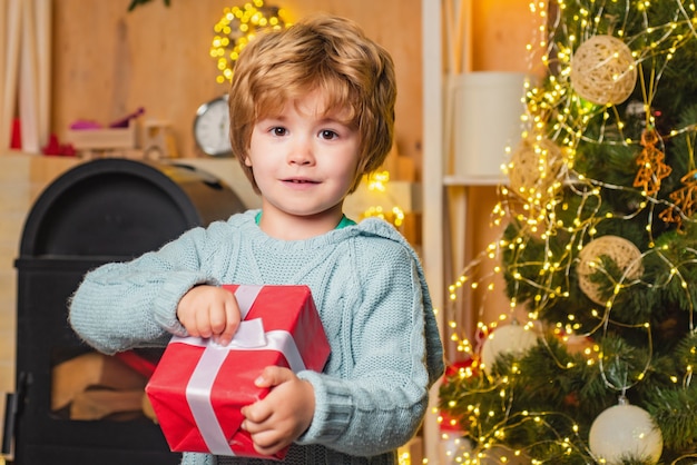 niño sosteniendo un regalo cerca de un árbol de navidad