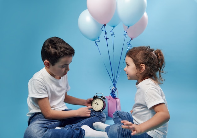 Niño sosteniendo un reloj despertador y mostrárselo a su hermana en la superficie de globos de colores