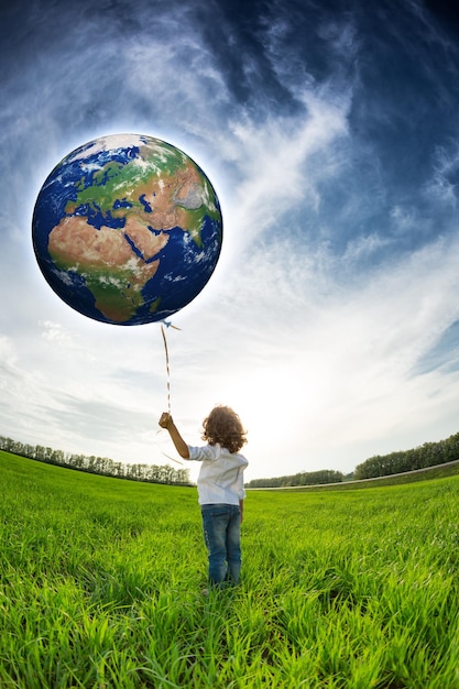 Niño sosteniendo la Tierra en la mano contra el cielo azul y el campo verde primaveral Elementos de esta imagen proporcionados por la NASA