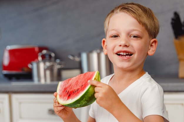 Niño sosteniendo un trozo de sandía en la cocina