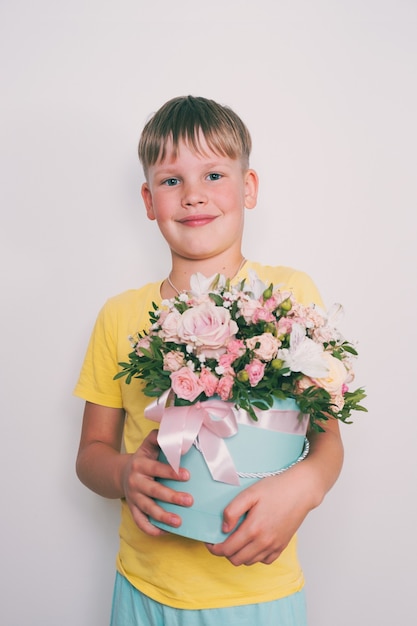 Foto el niño sostiene un arreglo floral en una caja redonda. un regalo para mamá. niño con un ramo de flores. teñido vintage.