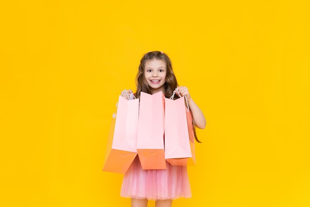 Un niño sostiene bolsas de papel con compras después de comprar Venta y compras para niñas pequeñas Una niña encantadora sostiene bolsas de regalo sobre un fondo amarillo aislado