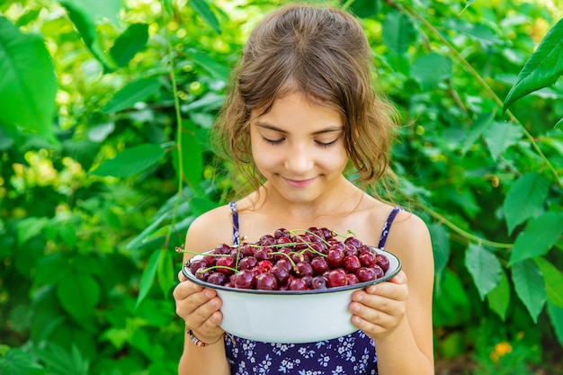 El niño sostiene un cuenco con cerezas en el fondo del jardín