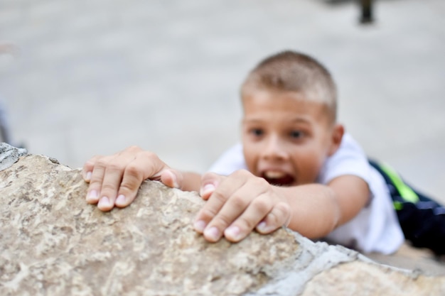 niño sostiene los dedos sobre el borde de la pared cayendo por un precipicio