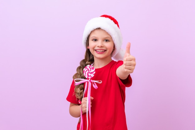 El niño sostiene un dulce de Navidad en un palo en sus manos y señala con el pulgar hacia arriba.