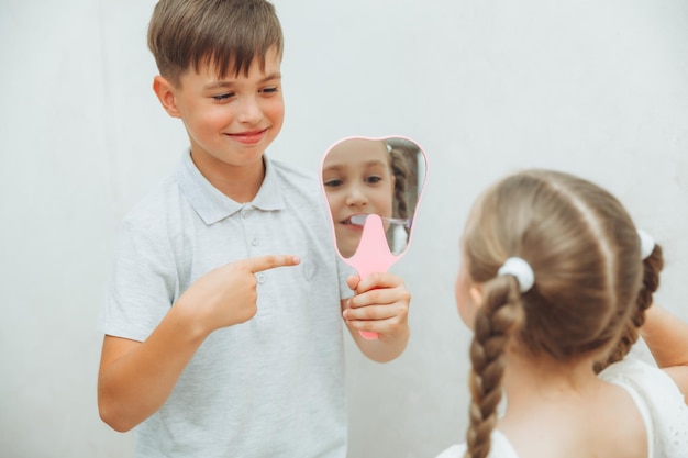 Un niño sostiene un espejo en el que una niña mira y se cepilla los dientes con un fondo blanco higiene y cuidado dental