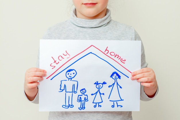 Un niño sostiene una imagen de una silueta familiar debajo del techo y las palabras se quedan en casa en casa