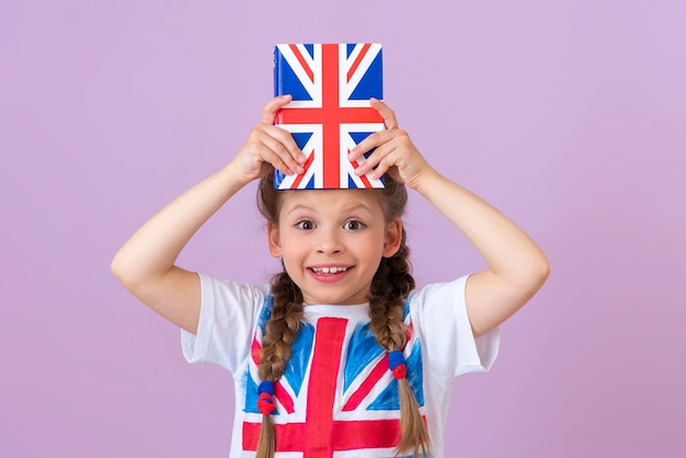 El niño sostiene un libro de texto de inglés sobre su cabeza y está feliz.