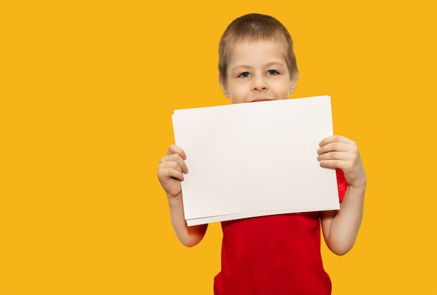 Un niño sostiene un papel sobre un fondo amarillo