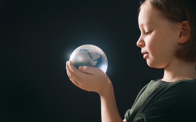 El niño sostiene el planeta en las manos sobre un fondo oscuro Concepto de vacaciones del Día de la Tierra